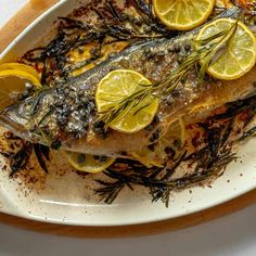 fish with lemons and herbs on a white plate, ready to be served in the oven