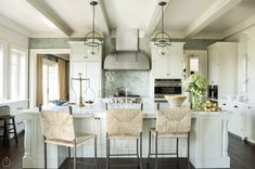 a large kitchen with white cabinets and wooden flooring, along with two bar stools