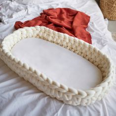 a white basket sitting on top of a bed next to a red blanket and a wicker basket