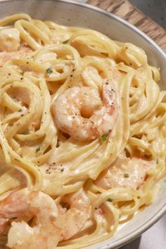 a bowl filled with pasta and shrimp on top of a wooden table