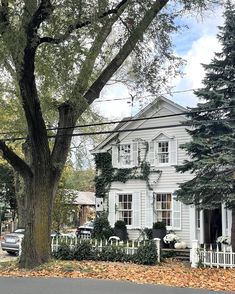 a large white house sitting on the side of a road next to a tree with lots of leaves