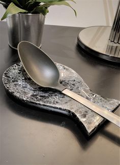 a silver spoon sitting on top of a marble slab next to a potted plant