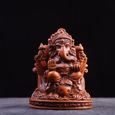 an elephant statue sitting on top of a wooden table next to a black background with the image of lord ganesh