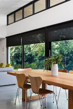 a dining room table with chairs and a couch in front of large windows that look out onto the woods