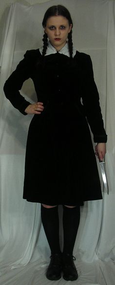 a woman in a black dress holding a knife and posing for the camera with her hands on her hips