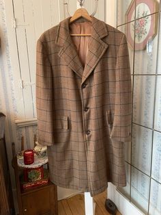 "This beautiful coat was, the label says, \"Tailored Expressly for Bill and Fred Regina\" (where we live!). It's made of medium weight, warm wool in medium brown and beige, with a windowpane check pattern in very dark brown and burnt orange. The coat has buttons on the front and cuffs, two outer pockets and two inner pockets, and is fully lined with coppery brown satiny lining. Please note that the lining has been repaired at some point; see photos. The measurements, taken with the coat lying flat, are: shoulder to shoulder, 20 inches; armpit to armpit, 23 inches; sleeves, 26 inches; length, 44 1/2 inches; bottom edge, 38 inches. In very good condition." Brown Long Wool Coat For Fall, Formal Long Brown Outerwear, Formal Brown Wool Coat With Long Sleeves, Brown Wool Coat For Fall, Fitted Brown Wool Coat, Formal Brown Wool Coat, Brown Wool Coat For Business, Business Brown Wool Coat, Brown Wool Coat For Winter Tailoring