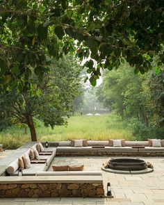 an outdoor seating area with benches and fire pit surrounded by trees in the middle of a field