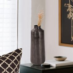 a black vase sitting on top of a wooden table next to a white and black pillow