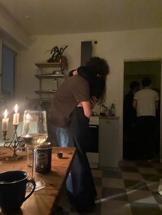 two people hugging each other in front of a table with wine glasses and candles on it