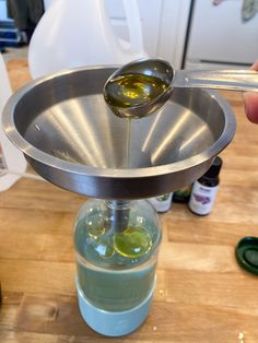 a person is pouring olive oil into a glass jar on a metal tray with a spoon