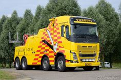 a yellow and red truck parked on the side of a road next to some trees