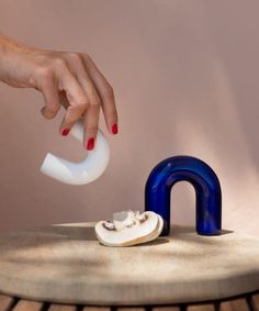 a woman's hand reaching for an object on top of a wooden table next to a blue and white faucet