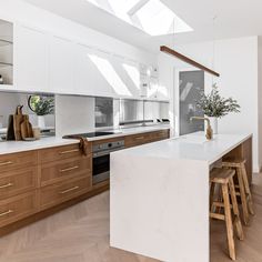 a kitchen with white counter tops and wooden stools in front of an island that has a potted plant on it