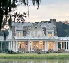 a large white house sitting on top of a lush green field next to a lake