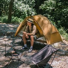 a man sitting in a tent next to some camping equipment