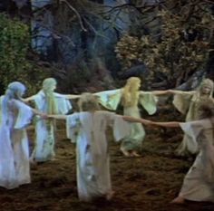 four women in white dresses are holding hands with each other while walking through the woods