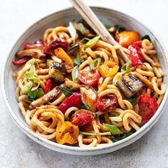 a bowl filled with noodles and vegetables on top of a white countertop next to a wooden spoon