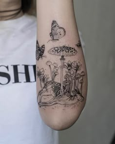 a woman's arm with tattoos on it and butterflies flying over the ground in the background