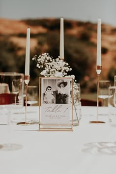 the table is set with wine glasses, candles and an empty photo frame on it