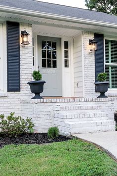 a white brick house with blue shutters and potted plants on the front porch