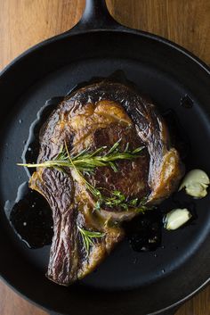 a piece of meat in a skillet with some herbs on the top and garlic on the side