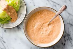 a bowl of dressing next to a plate of lettuce