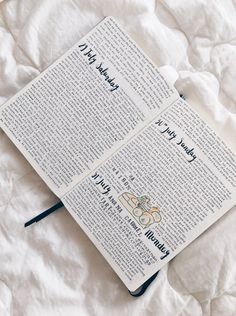 an open book sitting on top of a bed next to a white sheet with writing