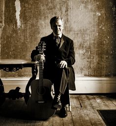 a man in a suit and tie sitting next to a guitar on a wooden floor