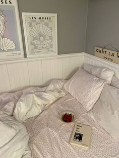 a white bed topped with pillows and a book on top of it next to two framed pictures