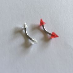 two small red and silver earrings on a white surface, one has an arrow shaped nose ring