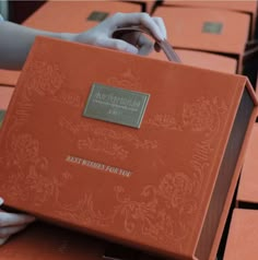 a person is holding an orange book in front of rows of red boxes with writing on them