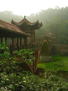 a bridge in the middle of a lush green field with trees and bushes surrounding it