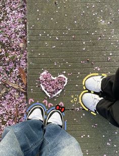 two people standing next to each other on a sidewalk with pink flowers in the background