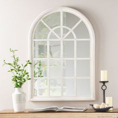 a table with a vase, candle and book on it next to a window that has an arched pane