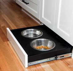 an open dog bowl on the floor in front of a kitchen counter with white cabinets