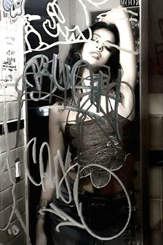 a woman standing in front of a mirror with graffiti on it's walls and writing all over her body