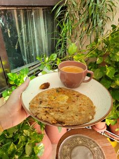 a person holding a plate with food on it and a cup of tea in front of them