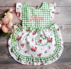 a green and white checkered dress with flowers on the bottom, sitting next to pink roses