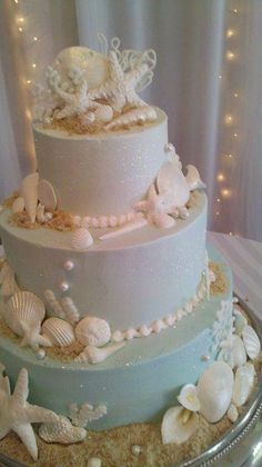 a three tiered wedding cake with sea shells and pearls on the bottom is displayed