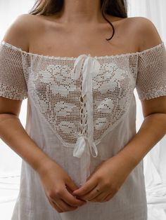 a woman is wearing a white top with lacy lace on it's shoulders and has her hands in her pockets