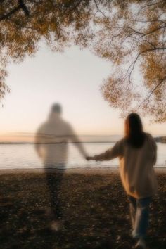 two people holding hands while walking near the water