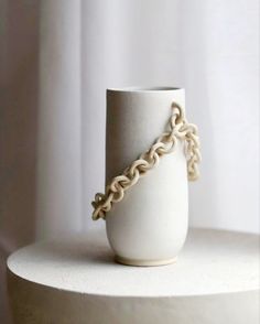 a white vase sitting on top of a table with a chain around it's neck