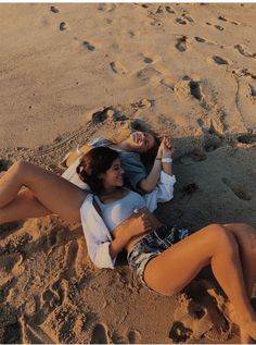 two women laying on the beach with their arms around each other