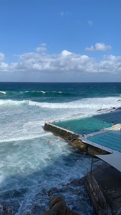 people are swimming in the ocean next to some rocks and water on a sunny day