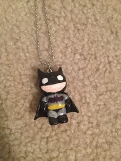 a necklace with a batman figure hanging from it's side on a carpeted surface