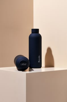 a blue bottle sitting on top of a white counter next to a black one - piece object