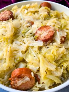 a white bowl filled with cabbage, sausage and other food on top of a blue table cloth