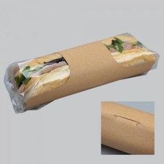 a sandwich wrapped in plastic and sitting on top of a cardboard box with the lid open