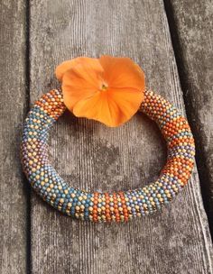 an orange flower sitting on top of a wooden bench next to a beaded bracelet