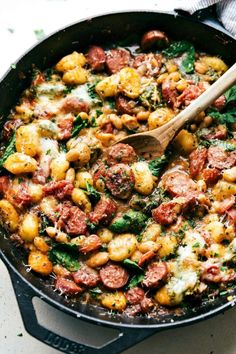 a skillet filled with sausage, potatoes and spinach on top of a table